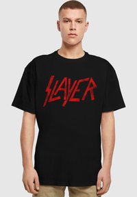 Černé bavlněné tričko s velkým červeným logem "SLAYER" v výrazném, ostrém písmu. Látka má hladkou strukturu a volný střih.