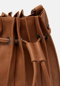 Primo piano di un cordino in pelle marrone con occhielli in metallo su una borsa in pelle texturizzata.