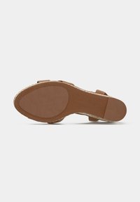 Semelle marron d'une sandale pour femme avec une texture au niveau du talon et de la balle, montrant un détail de bord tissé sur fond blanc.