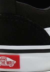 Zapatilla de lona negra con upper texturizado, suela blanca y logo rojo de "Vans Off The Wall" en el lateral. Presenta un ribete negro.