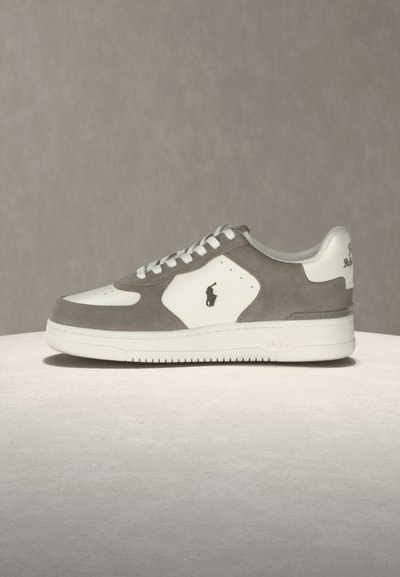 Χαμηλού τύπου αθλητικό παπούτσι σε λευκό και γκρι σουέτ με λευκή σόλα, κορδόνια και μικρό μαύρο λογότυπο αλόγου στην πλαϊνή επιφάνεια.