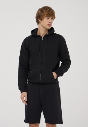 Czarny hoodie na zamek wykonany z mieszanki bawełny, z kapturem, sznurkami i przednimi kieszeniami, w połączeniu z czarnymi szortami. Gładka tekstura.