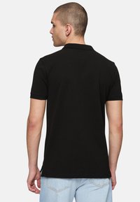 Svart pikétröja med korta ärmar, tillverkad av mjuk bomull, med klassisk krage och sidslitsar i fållen för ökad komfort.