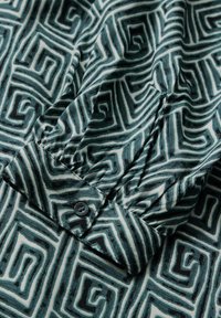 Mönstrad skjorta i grönt och krämfärgat med abstrakta geometriska mönster. Har en knappdetalj och en slät, texturerad tyg.