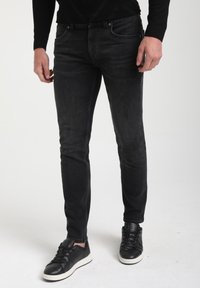 Mustad slim-fit teksad, millel on kulunud viimistlus, viis taskut ja keskmise kõrgusega vöökoht, koos mustade sidumisega tossudega.
