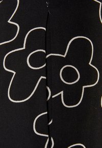 Tissu noir avec de grandes fleurs à cinq pétales blanches en contour, présentant des centres circulaires, avec une couture verticale au milieu.