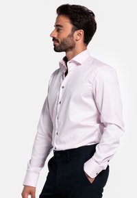 Lichtroze overhemd met een button-down kraag, zilveren knopen en contrasterende, patroonachtige voering die zichtbaar is bij de kraag. Aansluitend model.
