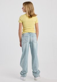 Vaaleankeltainen istuva t-paita, yhdistettynä löysästi istuviin vaaleansinisiin farkkuihin, joissa on takataskut ja pehmeä rakenne. Valkoiset lenkkarit.