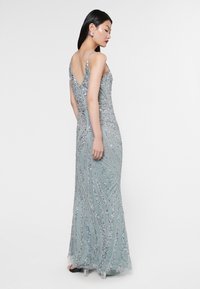 Abito da sera lungo decorato con paillettes in blu chiaro, con schiena a V, silhouette aderente e motivo di perline a onde. Sandali con tacco trasparente.
