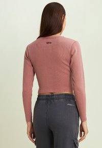 Top a maniche lunghe, corto, in tessuto a costine colore rosa cipria. Presenta un discreto logo Disney nero sul retro. Abbinato a pantaloni jogger grigi.