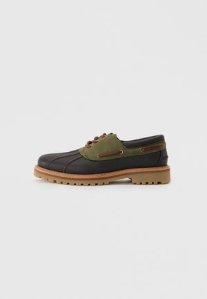 Black and green lace-up shoe with a rounded toe, textured leather and fabric upper, and a rugged, brown rubber sole. Red eyelets detail.