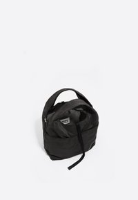 Czarny plecak z nylonu o zaokrąglonym kształcie, z górną rączką i zapięciem na zamek. Wewnątrz widać miękką podszewkę z metką. Minimalistyczny design.
