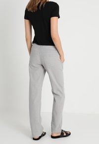 Szare bawełniane spodnie o prostym kroju, z bocznymi kieszeniami i detalami na tyle. W połączeniu z czarną bluzką z krótkim rękawem i sandałami.