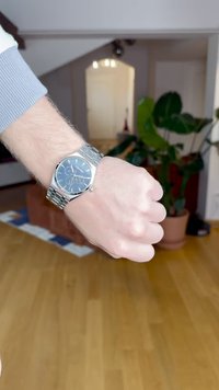 Ασημένιο ρολόι από ανοξείδωτο ατσάλι με μπλε καντράν, τρεις υποκαντράν και υφασμένο λουράκι, φορεμένο σε καρπό με κλειστή γροθιά.