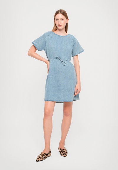 Τζιν φόρεμα με κοντά μανίκια, ζωνάκι στη μέση, και ίσια γραμμή. Ανοιχτό μπλε χρώμα με φθαρμένες λεπτομέρειες στο τελείωμα. Φορεμένο με παπούτσια επίπεδης σόλας με λεοπάρ σχέδιο.