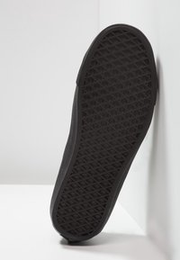 Černá podrážka boty s texturovaným vzorem vaflí, s hladkým okrajem a zakřiveným tvarem, umístěná na světlém pozadí.