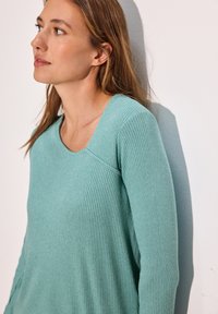 Grön ribbad långärmad topp med rund halsringning och sömdetaljer, tillverkad av mjukt tyg med en slät yta.