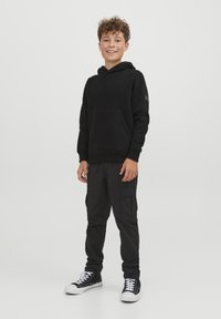 Felpa nera con tasca frontale, abbinata a pantaloni cargo neri con tasche laterali. Completato con sneakers basse nere e bianche.