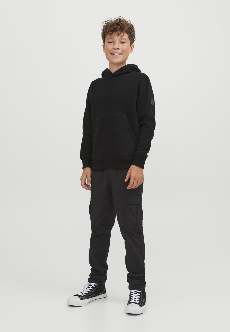Felpa nera con tasca frontale, abbinata a pantaloni cargo neri con tasche laterali. Completato con sneakers basse nere e bianche.