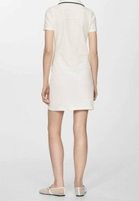 Robe à manches courtes de couleur crème avec un col à revers et un bord noir. Tissu lisse, coupe ajustée, longueur mi-cuisse. Associée à des ballerines claires.