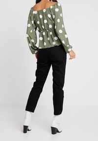 Top peplum verde a pois con maniche lunghe, pantaloni neri a vita alta e stivali bianchi con tacco alla caviglia. Tessuto liscio, vestibilità comoda, design scivolato sulle spalle.
