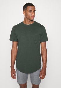 Donkergroene t-shirt met korte mouwen, ronde hals en gebogen zoom, gedragen met grijs geruite shorts. Glad katoen, casual pasvorm.