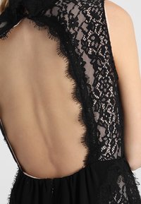 Robe noire présentant un décolleté profond dans le dos, un délicat bord en dentelle, un corsage ajusté avec une jupe fluide et une fermeture éclair discrète.