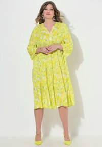 Jasnożółta, wzorzysta sukienka z dekoltem w serek, rękawami typu nietoperz i warstwową spódnicą. W zestawie z pasującymi, żółtymi, szpiczastymi szpilkami.