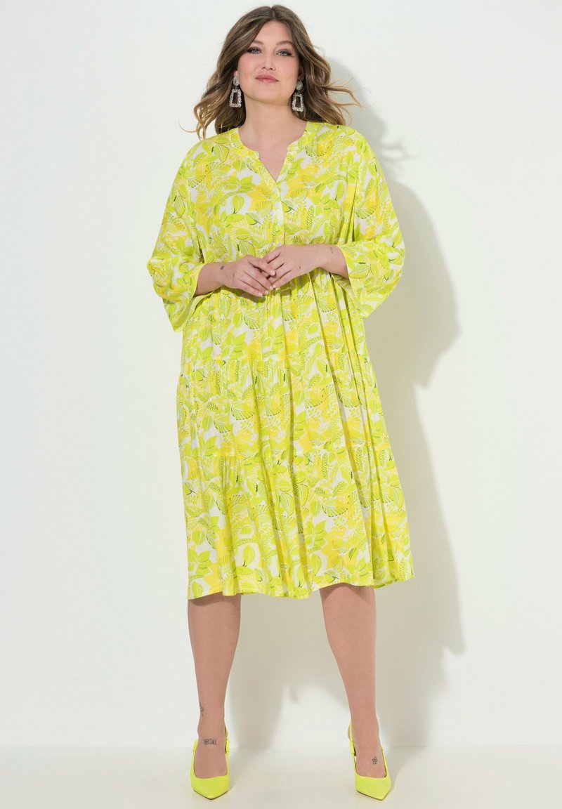 Jasnożółta, wzorzysta sukienka z dekoltem w serek, rękawami typu nietoperz i warstwową spódnicą. W zestawie z pasującymi, żółtymi, szpiczastymi szpilkami.