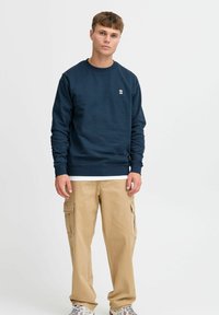 Sweatshirt bleumarin cu guler și manșete ribbate, asociat cu pantaloni cargo bej care au buzunare laterale și un design cu picioare drepte.