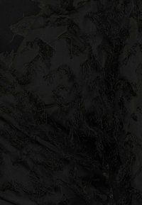 Una tela negra con acentos texturizados y deshilachados crea un aspecto en capas. El material es ligero, con un sutil brillo contra un fondo mate.