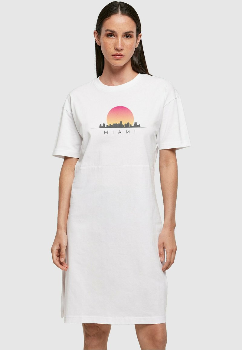 Fehér pamut pólóruha rövid ujjakkal, elülső részén színes Miami látképet és gradient napmintázatot ábrázoló grafikával.