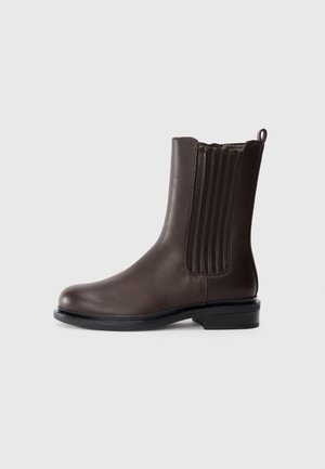 Bottine en cuir brun avec un bout arrondi, des panneaux latéraux élastiques et une languette ; le petit talon noir apporte un contraste au design.