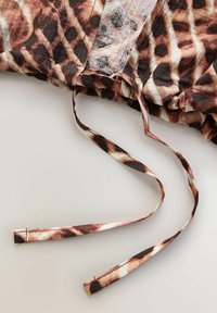 Șnur cu țesătură cu imprimeu animalier, fiind pete de leopard maro, negru și bej pe marginea încrețită a unei haine.