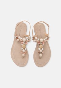 Sandale bej cu talpă plată, având o ornamentație decorativă din mărgele și pietre pe partea superioară a baretei pentru degetul mare. Include și o baretă ajustabilă pentru gleznă.