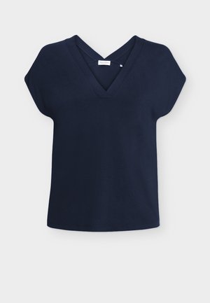 Laivastonsininen lyhythihainen pusero V-pääntiellä ja hillityllä ristikkäisellä yksityiskohdalla pääntiessä, tasaisesti aseteltu vaalealle taustalle.