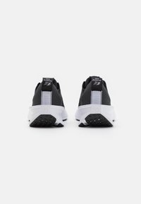 Sorte sportssko med et tekstureret mesh-overdel, hvid mellemsål og sort gummi-ydersål. Har et logo på bagsiden og en polstret krave.