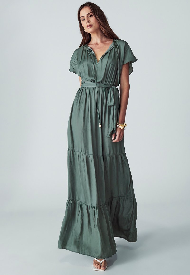Maxi šaty v tlumené zelené barvě, lehký materiál, vícestupňový design, volné krátké rukávy, stahovací pas, zakončeno bočními rozparky a hladkým povrchem.