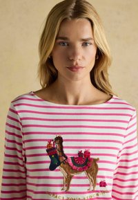 Prúžkované dlhé rukávy top s ružovými a bielymi pruhmi. Obsahuje vyšívanú alpacku nesúcu darčeky a ponožku. Mäkká štruktúra materiálu.