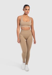 Beige urheiluliivin ja korkeavyötäröisten leggingsien yhdistelmä joustavasta materiaalista. Muotoonompelu ilman näkyviä kuvioita tai metalliosia.