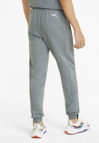 Gray sweatpants with ribbed side panels and elastic waistband, paired with white and red athletic shoes featuring blue accents.