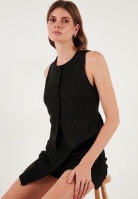 Vesta neagră fără mâneci, cu guler rotund, dotată cu nasturi în față, două buzunare laterale și un finisaj texturat. Design îndrăzneț și ajustat.