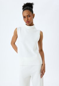Top sans manches blanc en texture côtelée, avec une coupe décontractée et un ourlet droit. Design minimaliste, idéal pour les superpositions.