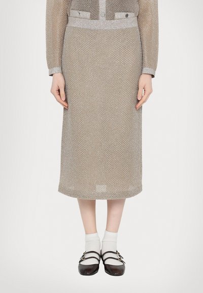 Vestido de punto beige hasta la rodilla con un patrón texturizado y detalles plateados; incluye un cuello estructurado y botones. Combinado con zapatos negros y calcetines blancos.