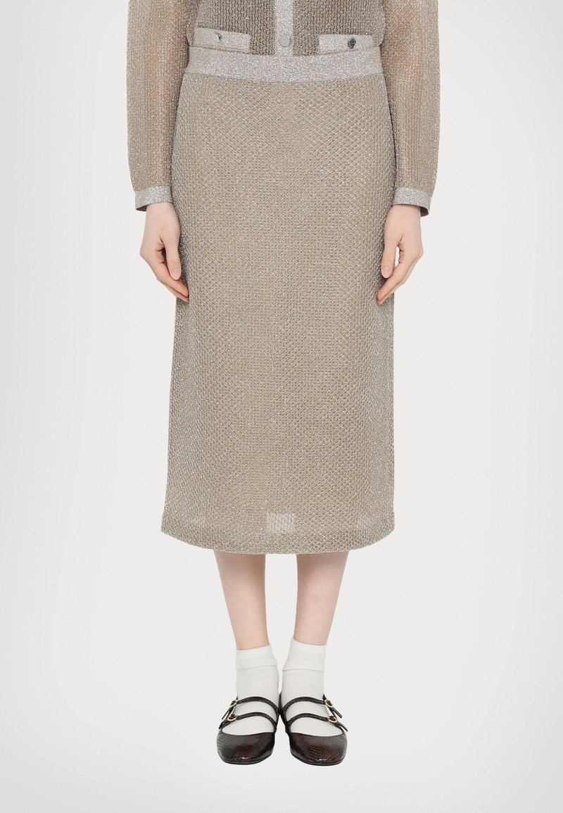 Vestido de punto beige hasta la rodilla con un patrón texturizado y detalles plateados; incluye un cuello estructurado y botones. Combinado con zapatos negros y calcetines blancos.