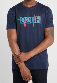 T-shirt in cotone blu navy con un audace logo "HUGO" multicolore sul petto. Maniche corte e scollatura a girocollo.
