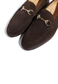 Braune Wildleder-Loafer mit klassischem Design, gesticktem Detail und einer goldfarbenen Kettenakzent oben. Flache Sohle für bequemes Tragen.