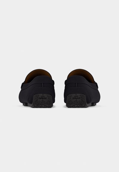 Mocassins en cuir noir avec semelles en caoutchouc texturées, vus de dos montrant le nom de la marque "Bally" sur chaque semelle.