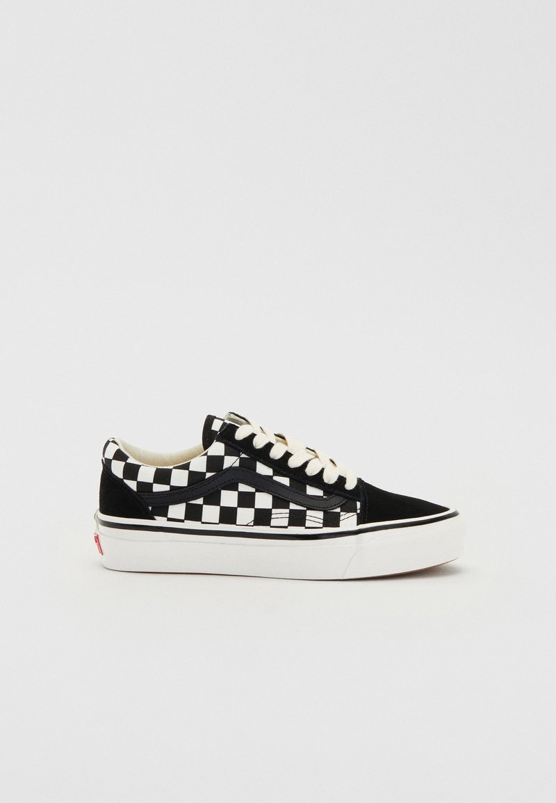Baskets basses à damier noir et blanc avec des lacets blancs, des accents noirs et une semelle blanche épaisse sur un fond clair uni.