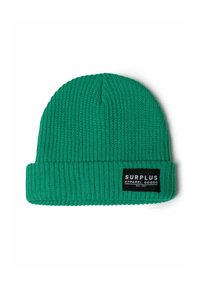 Zeleni pleteni beanie s rebrastom teksturom i preklopom. Sadrži crnu oznaku s tekstom "SURPLUS APPAREL GOODS".